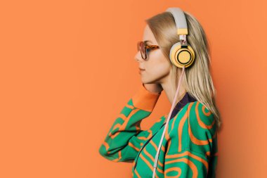 Turuncu arka planda gözlüklü, kulaklıklı ve bluzlu 80 'lerin şık kadını.