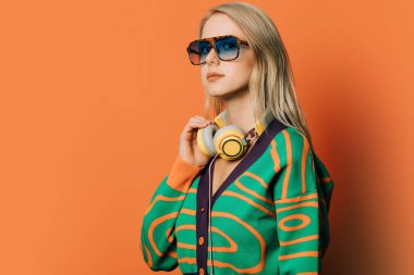 Turuncu arka planda gözlüklü, kulaklıklı ve bluzlu 80 'lerin şık kadını.