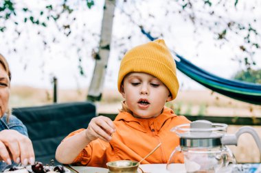 Sarı şapkalı küçük çocuk köy bahçesindeki masada oturuyor.