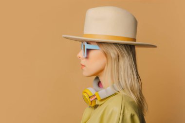 Stylish 80s woman in eyeglasses, headphones and hat on brown background
