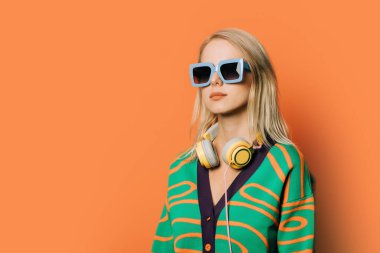 Turuncu arka planda gözlüklü, kulaklıklı ve bluzlu 80 'lerin şık kadını.