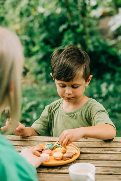 Little boy with a mother eats macaron cookies in outdoor