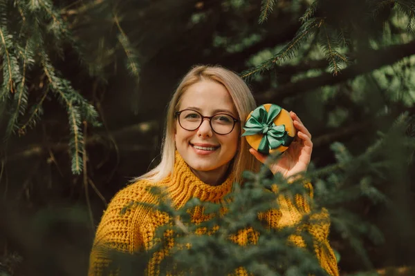 Stylish blond hair woman in sweater with Cristmas gifts stay near pine tree