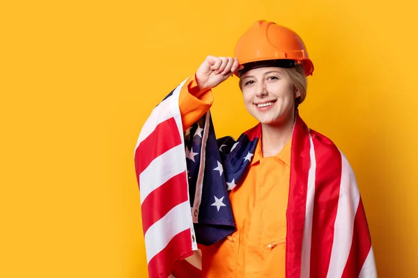 ヘルメットとオレンジの女性建設労働者黄色の背景に米国の旗と全体 — ストック写真