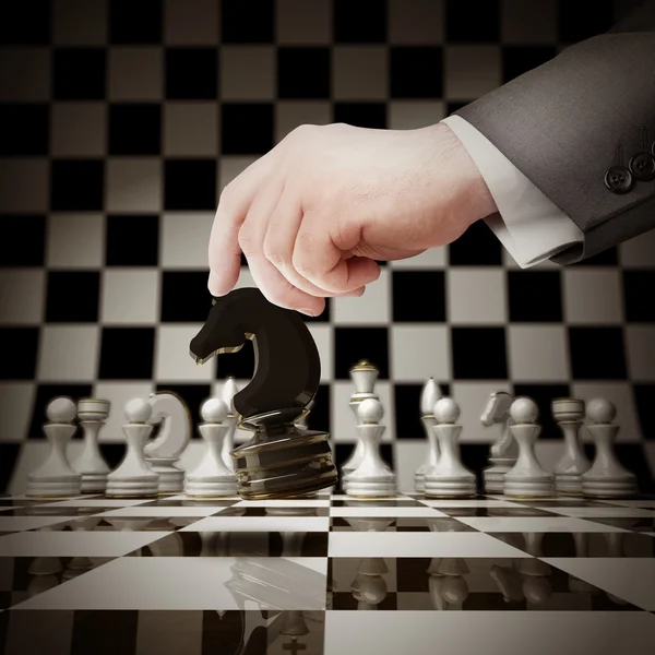 Ręka trzyma szachy biała postać na szachownicy — Zdjęcie stockowe