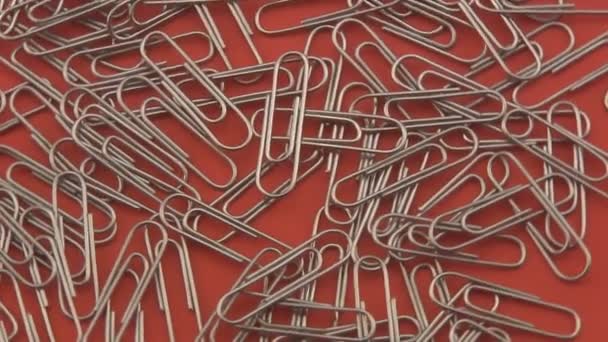Silver paper clips rotating on a red background. — Stock Video