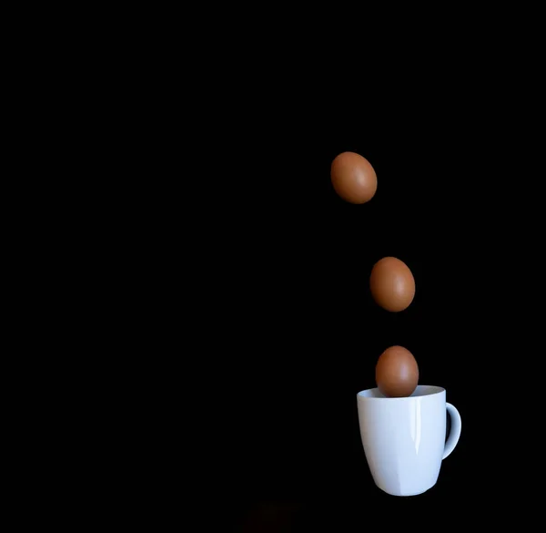 Algunos Huevos Cayendo Una Taza Blanca Sobre Fondo Negro Pascua —  Fotos de Stock