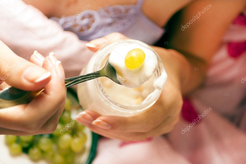 The woman eats yogurt with grapes