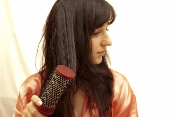 A mulher penteia o cabelo o secador de cabelo — Fotografia de Stock