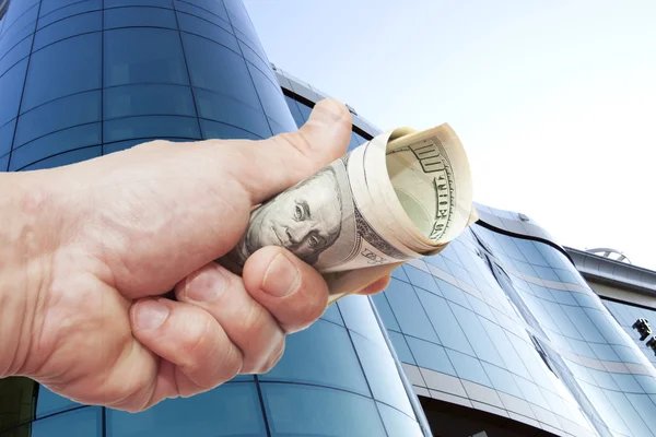 Hand with notes of dollars against office building — Stock Photo, Image