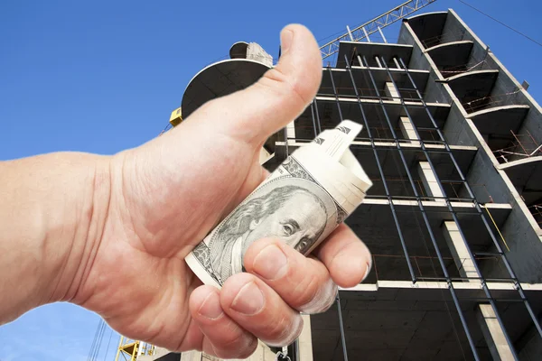 Рука с долларами против строящегося дома — стоковое фото