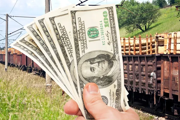 Мужская рука с долларами США против поезда — стоковое фото