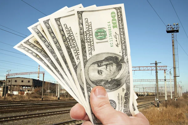 Рука с долларовыми купюрами против железной дороги — стоковое фото