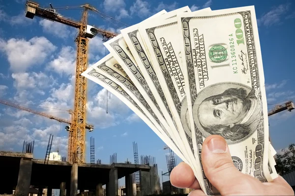 Hundred dollar notes of the USA in a hand against a construction — Stock Photo, Image