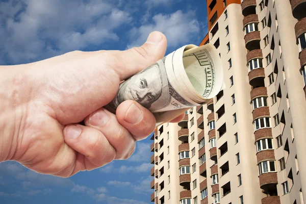 Долларовые купюры в руке против жилого дома на высоком этаже — стоковое фото
