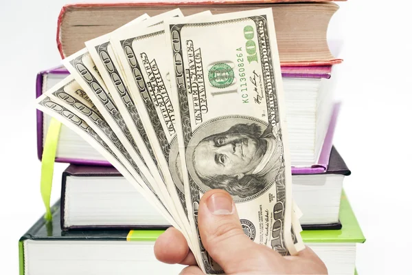 Hand with notes of US dollars against books — Stock Photo, Image