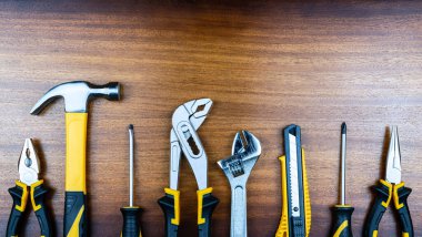 Ev işleri için çeşitli araçlar kahverengi ahşap tahtaların arka planında bir sırada gösterilir