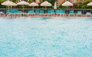 Güneşli yatakların arka planında ve dinlenmek için şemsiyelerde temiz su bulunan havuz.