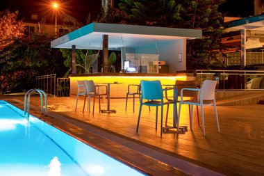Otelin havuzunda neon ışıkları, masaları ve sandalyeleri olan bir gece barı.