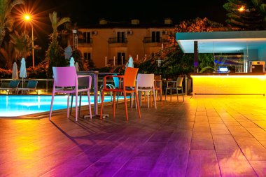 Otelin havuzunda neon ışıkları, masaları ve sandalyeleri olan bir gece barı.