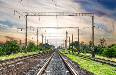 Güneş batımının arka planında üç raylı, güzel gökyüzü olan elektrikli demiryolu.