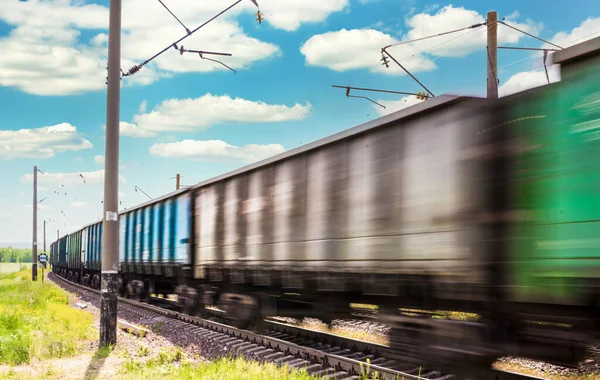 在电气化的铁路上 在蓝天和云彩的衬托下 载满货车的火车在行驶 图库图片