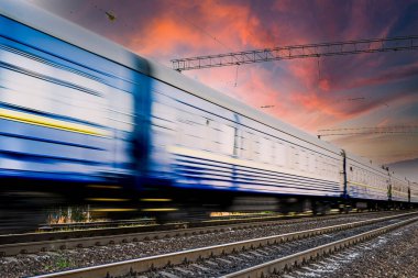 Mavi tren yolcu vagonları, güzel gökyüzü ve günbatımı arka planında hızlı bir hareketle bulanıklaştı.