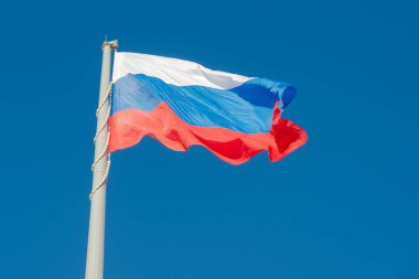 Rus bayrağı mavi gökyüzüne karşı rüzgarda dalgalanıyor.