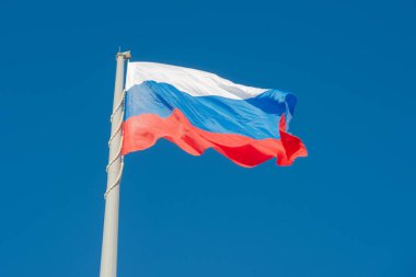 Rus bayrağı mavi gökyüzüne karşı rüzgarda dalgalanıyor.