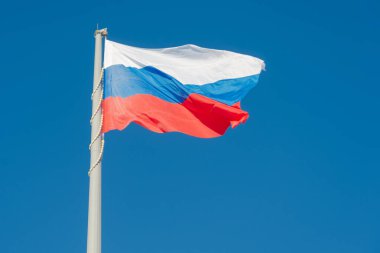 Rus bayrağı mavi gökyüzüne karşı rüzgarda dalgalanıyor.
