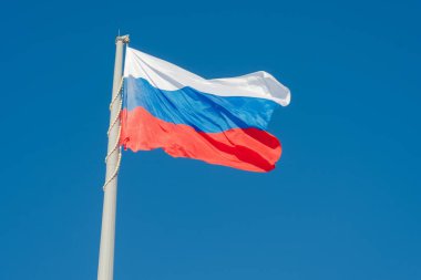 Rus bayrağı mavi gökyüzüne karşı rüzgarda dalgalanıyor.