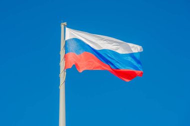 Rus bayrağı mavi gökyüzüne karşı rüzgarda dalgalanıyor.