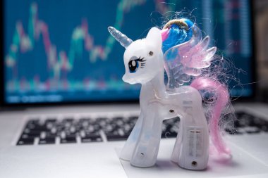 Dizüstü bilgisayardaki tek boynuzlu at oyuncağı borsa grafik arka planında