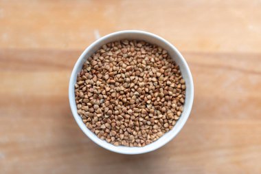 Tahta arka planda izole edilmiş beyaz seramik kasede kuru karabuğday. Dökülmüş karabuğday.