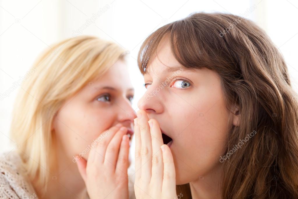 Blonde girl telling a secret to her best friend