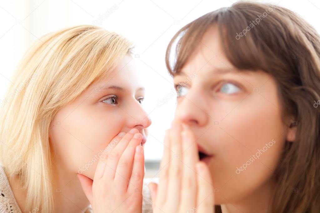 Blonde girl telling a secret to her best friend