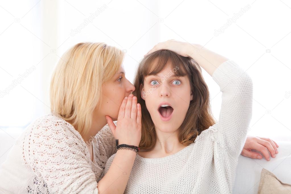 Blonde girl telling a secret to her best friend