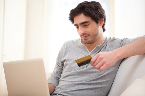 Entspannter junger Mann bezahlt online mit Kreditkarte auf Sofa — Stockfoto