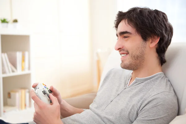 Joven hombre atractivo jugando videojuegos en línea en un sofá — Foto de Stock