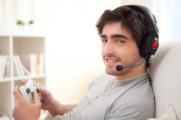 Joven hombre atractivo jugando videojuegos en línea en un sofá —  Fotos de Stock