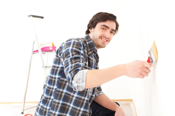 Aantrekkelijke jonge man schilderij een muur in zijn nieuwe appartement — Stockfoto