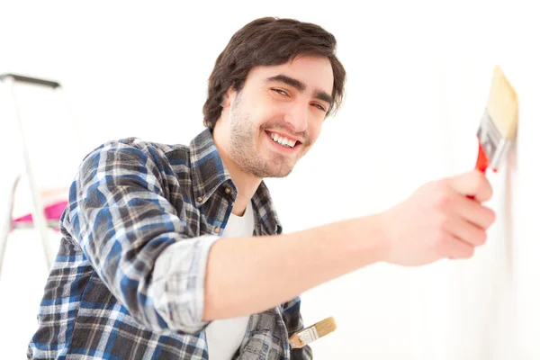 Aantrekkelijke jonge man schilderij een muur in zijn nieuwe appartement — Stockfoto