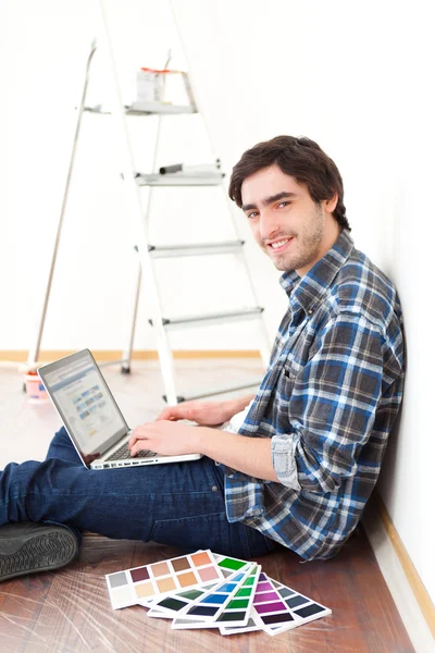 Νεαρός άνδρας, χρησιμοποιώντας φορητό υπολογιστή ενώ επιλέγοντας το χρώμα του διαμέρισμά — Φωτογραφία Αρχείου