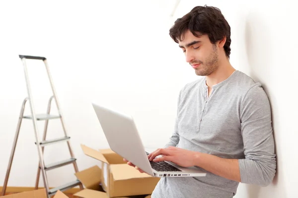 Beau jeune homme dans son nouvel appartement en utilisant un ordinateur portable — Photo