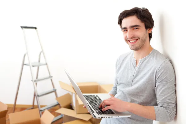 Schöner junger Mann in seiner neuen Wohnung mit Laptop — Stockfoto