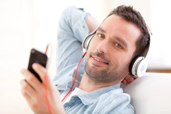 Jovem homem relaxado ouvindo música em um sofá — Fotografia de Stock