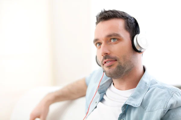 Jovem homem relaxado ouvindo música em um sofá — Fotografia de Stock