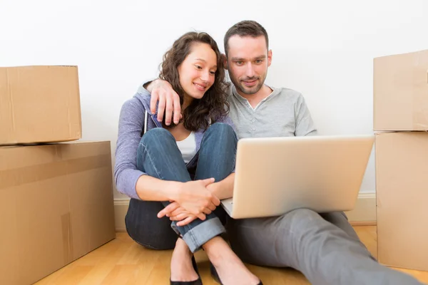 Young couple using laptop while moving in new flat — Stock Photo, Image