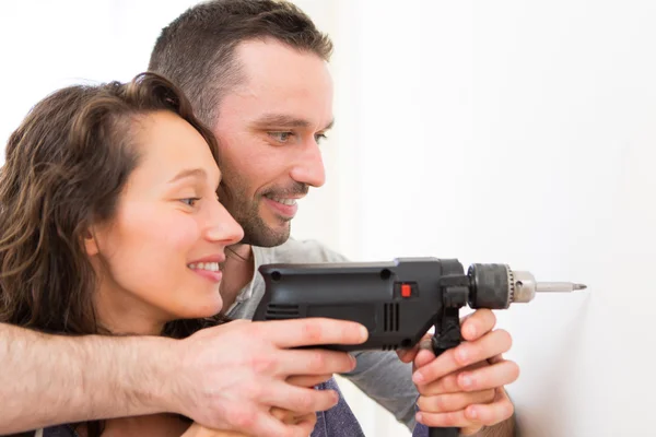 Hombre atractivo ayudando a su novia usando un taladro — Foto de Stock