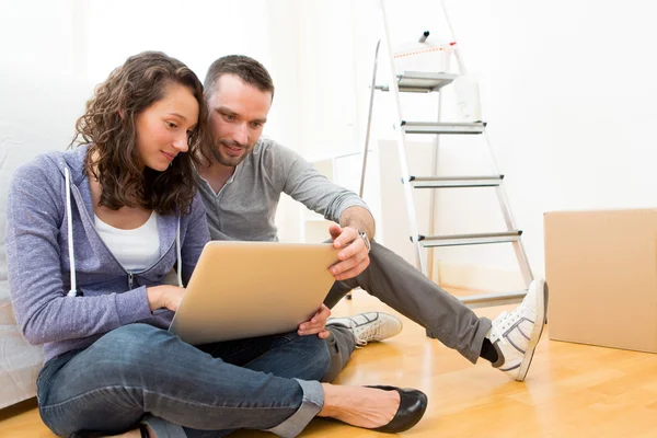 Young couple using laptop while moving in new flat — Stock Photo, Image